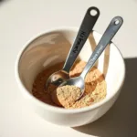 Chebe powder for hair growth, displayed in a bowl with measuring spoons.