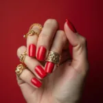 A hand with candy red nails adorned with gold rings and bracelets, illustrating how the color complements jewelry and accessories.