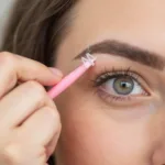 Woman using an eyebrow razor tool to shape her brows.